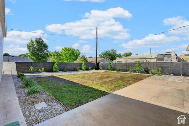Expansive outdoor space featuring a concrete patio, a section of new grass, and a gravel border with young trees and shrubs