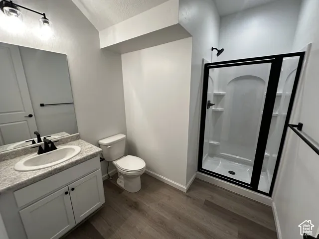Wood-finish flooring, white vanity with integrated sink, black hardware throughout, and a shower with a black-framed glass enclosure