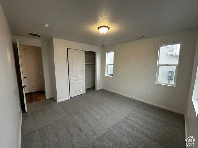 Carpeted flooring, white walls, two windows, and a sliding door closet with shelving