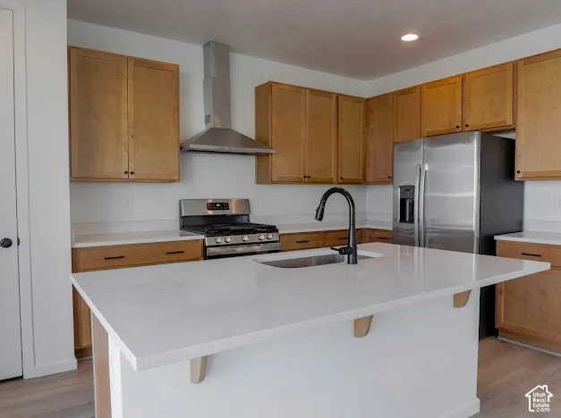 Kitchen featuring light wood cabinetry, stainless steel appliances, a center island with an undermount sink, and light-toned countertops