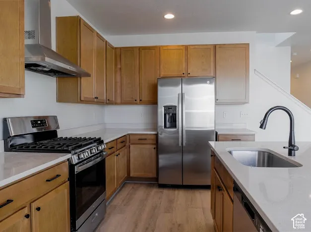 Kitchen featuring light wood cabinetry, stainless steel appliances, light-toned countertops, wood-finish flooring, and a stainless steel sink with a matte black faucet