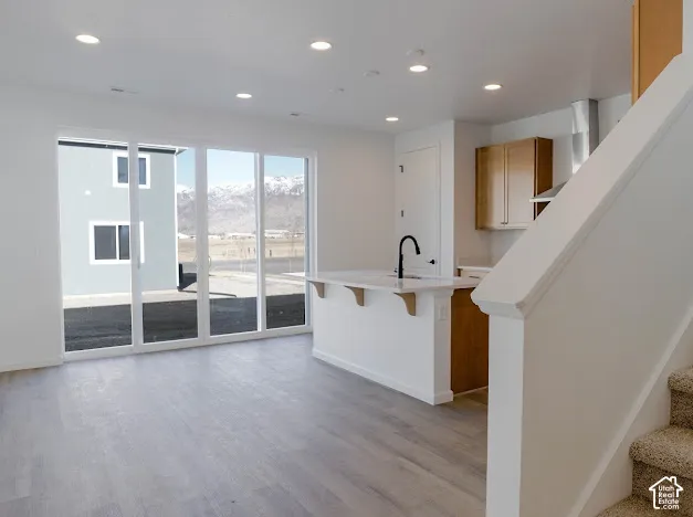 Spacious room with light wood-finish flooring, recessed lighting, and a white kitchen island featuring a black faucet