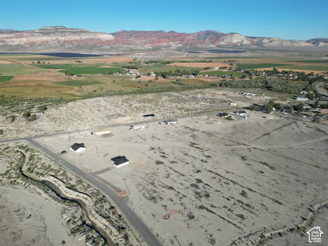 Expansive undeveloped land featuring a paved road, scattered structures, and distant mountainous terrain