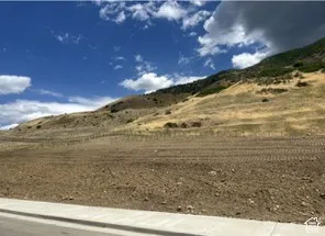 Expansive land parcel with graded terrain, a paved road, and concrete sidewalk