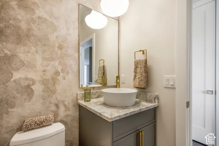 Pedestal vessel sink with gold-tone faucet, gray vanity with gold-tone hardware, marble-look countertop, and decorative wall covering