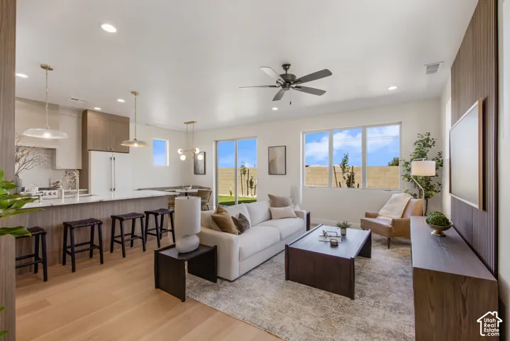 Open-concept living area with light wood-finish flooring, a contemporary ceiling fan, and large windows