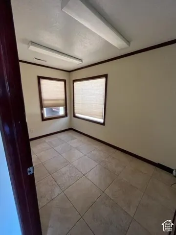 Neutral toned tile flooring, two windows with blinds, and white walls