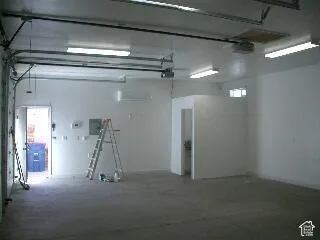 Concrete flooring, multiple fluorescent ceiling light fixtures, white walls, and a separate enclosed utility area
