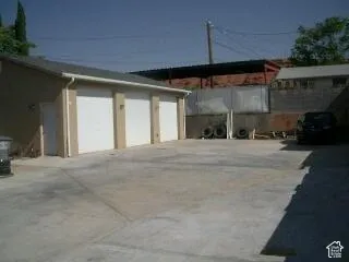 Three garage bays with white roll-up doors, a side entry door, and concrete hardscaping