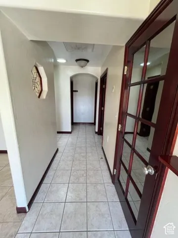 Hallway featuring square tile flooring, rich wood-finish doors with glass panels, an arched doorway, and recessed lighting