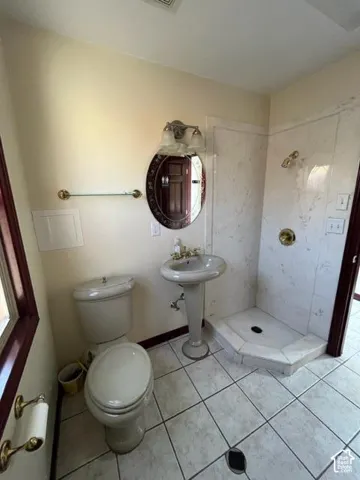 Pedestal sink with brass-finish faucet, toilet, and a tiled walk-in shower with brass-finish fixtures