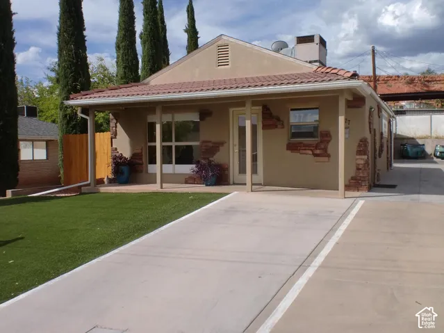 Stucco exterior with decorative stone accents, covered front porch, concrete driveway, and artificial turf lawn
