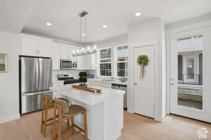 Modern kitchen featuring a center island with a light-toned countertop, stainless steel appliances, white cabinetry, and wood-finish flooring