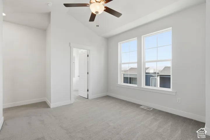 Vaulted ceiling with a ceiling fan, light gray carpet, and two large windows with white trim