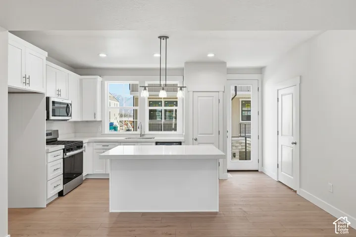 Kitchen featuring white shaker cabinetry, stainless steel appliances, a center island with a light-toned countertop, and wood-finish flooring