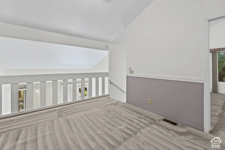 Cathedral ceiling with white finish, carpeted flooring, and white railing overlooking the lower level