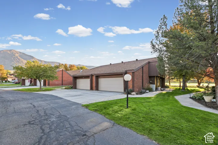 Brick exterior with a brown roof, attached two-car garage, concrete driveway, and a concrete pathway