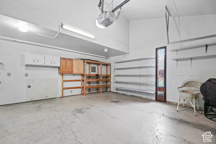 Attached garage featuring concrete flooring, overhead fluorescent lighting, a garage door opener, built-in shelving, and wall-mounted cabinetry