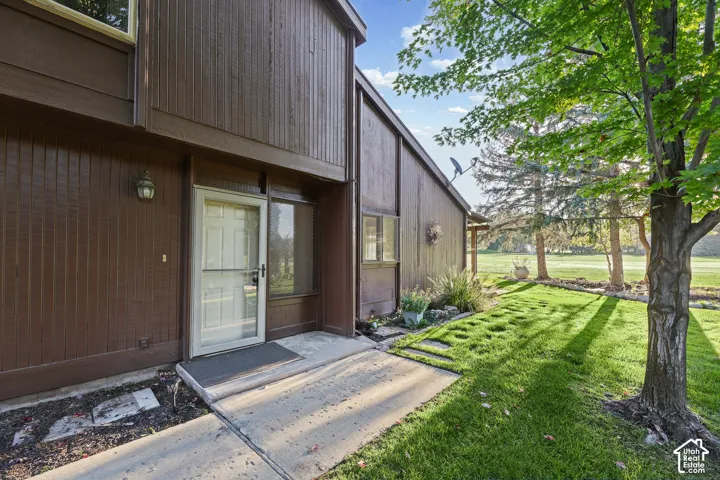Brown wood-sided exterior with white entry door, concrete pathway, and green lawn featuring stepping stones
