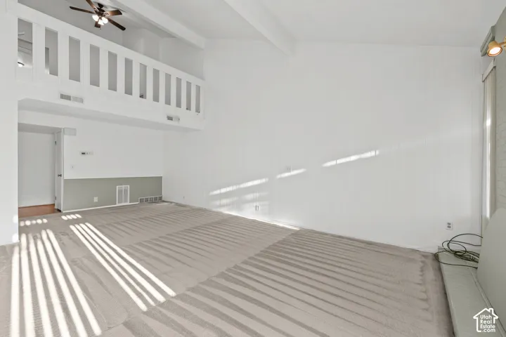 Vaulted ceiling, ceiling fan, white paneled walls, gray carpet, interior balcony with white railing