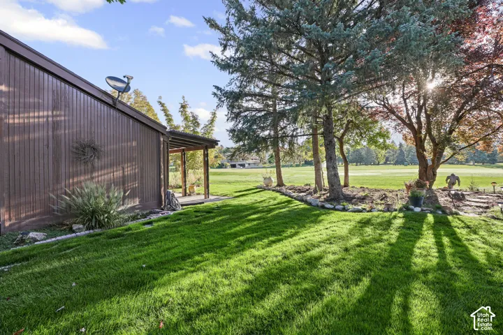 Expansive green lawn, mature trees, landscaped garden bed, covered patio, and board-and-batten siding