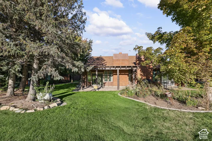 Expansive yard with mature trees, a stone-lined garden bed, and a brick exterior with a wood pergola