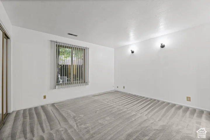 Wall-to-wall carpeting, window with vertical blinds, wall-mounted light fixtures, and a mirrored closet door