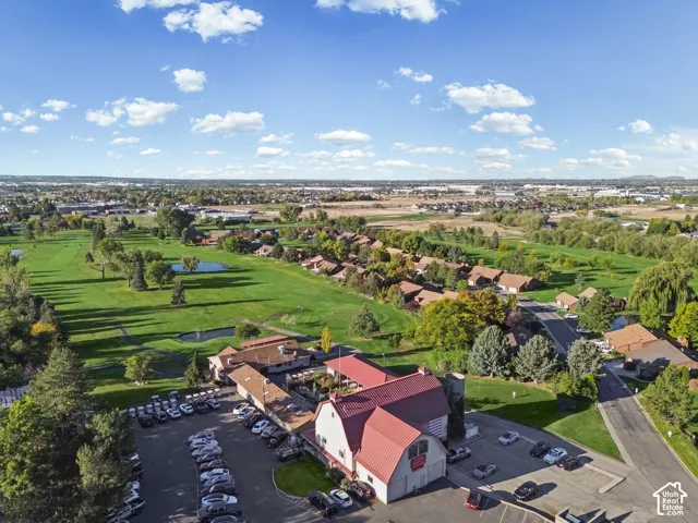 Aerial perspective showcasing a sprawling golf course, residential properties, an expansive parking area, and a building featuring a red roof and white siding