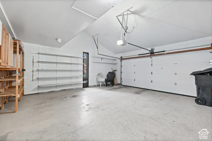 Spacious garage featuring a concrete floor, built-in shelving, an automatic garage door opener, and a side access door
