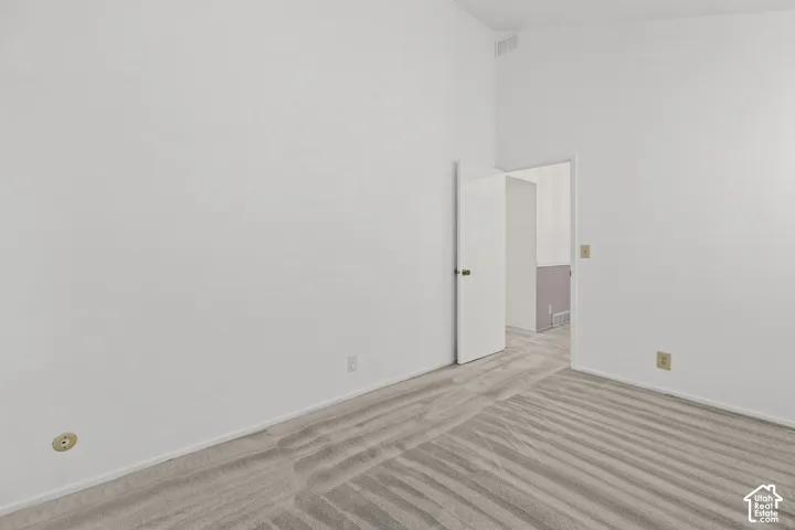 Vaulted ceiling, neutral wall paint, light-toned carpeting, and a white interior door