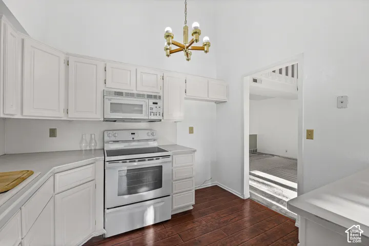 Vaulted ceiling, wood-finish flooring, white cabinetry, light-toned countertops, and an integrated microwave