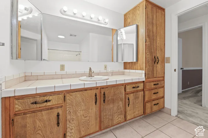 Extended vanity with wood-finish cabinetry, integrated basin sink, and tile countertop