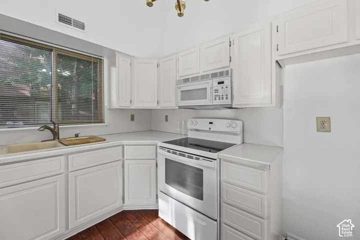 White cabinetry with matching appliances, solid surface countertops, and wood-finish flooring