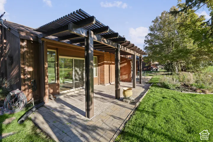 Paved patio with a large pergola, sliding glass doors, and a manicured lawn
