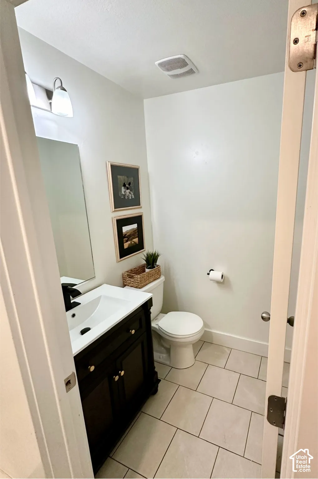 Bathroom featuring a dark wood-finish vanity with a white basin and matte black faucet, a rectangular mirror, and light-toned tile flooring