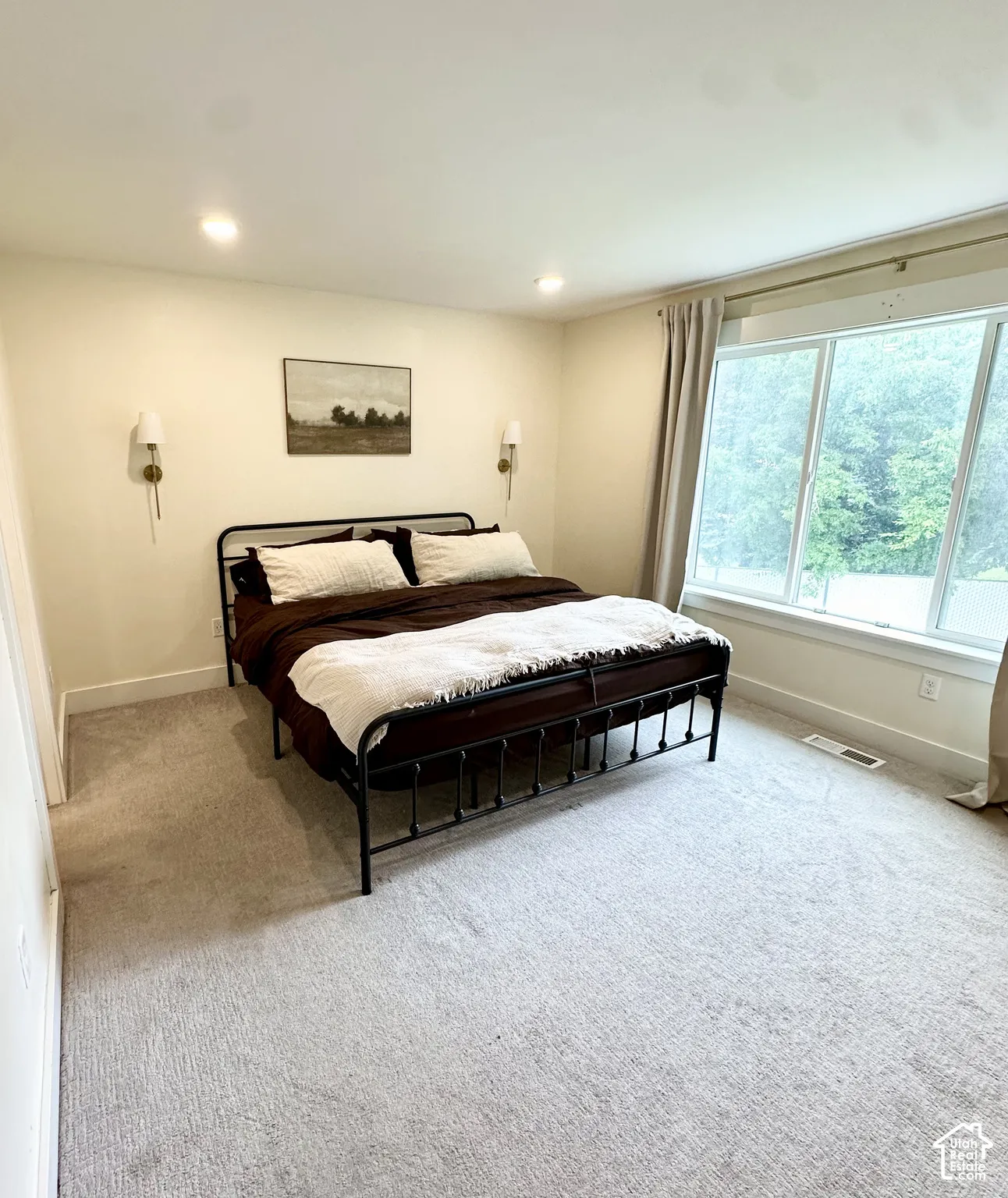 Recessed ceiling lighting, wall-mounted sconces, large window, and light-toned carpeting