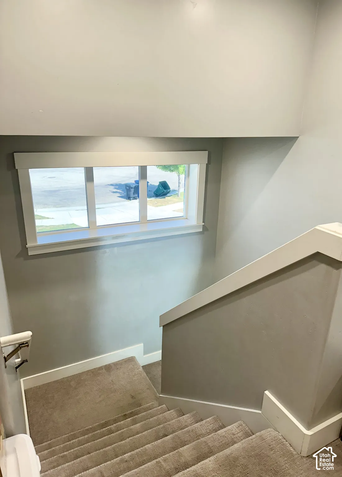 Staircase with plush carpeted treads, a solid wall-mounted handrail, a white framed window, and neutral wall paint