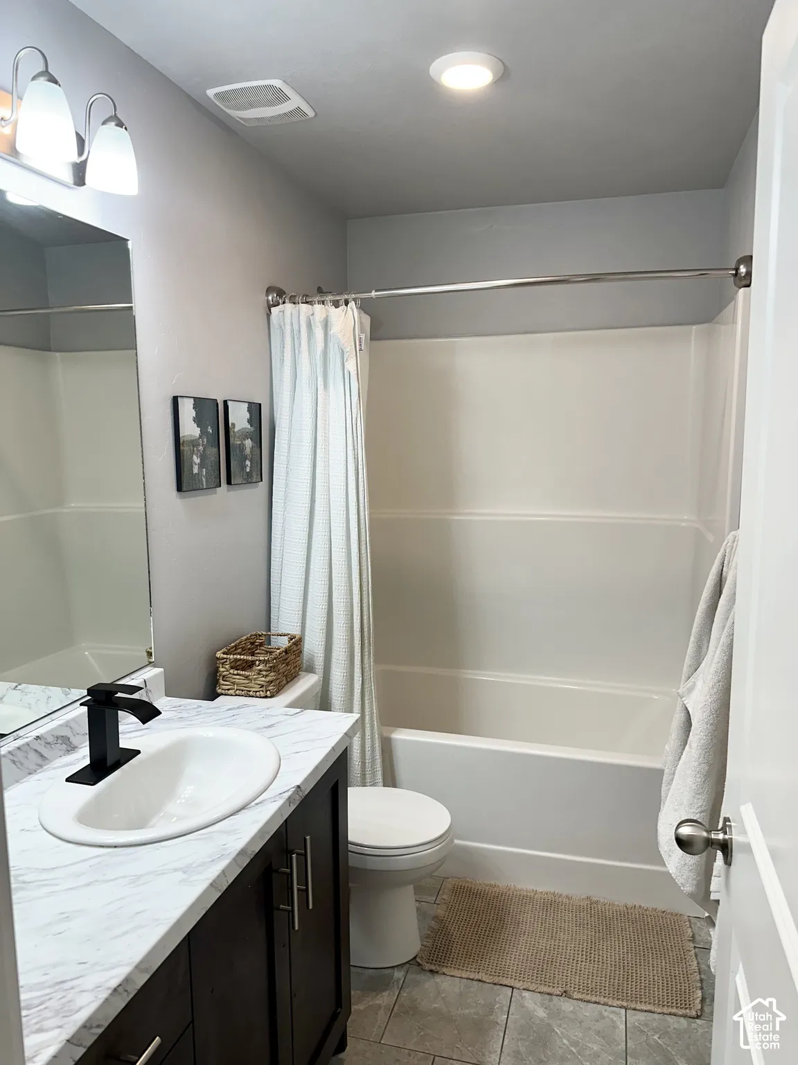 Bathroom featuring a vanity with a white faux marble countertop, dark wood-finish cabinetry, an undermount sink with a matte black faucet, and a white tub with shower