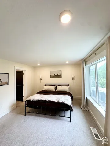 Recessed ceiling lighting, wall-mounted sconces, large window, dark paneled door, and neutral carpeting