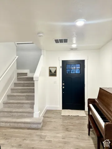 Wood-finish flooring, staircase with carpeted treads, white painted walls, recessed lighting, and a dark paneled door with glass inserts