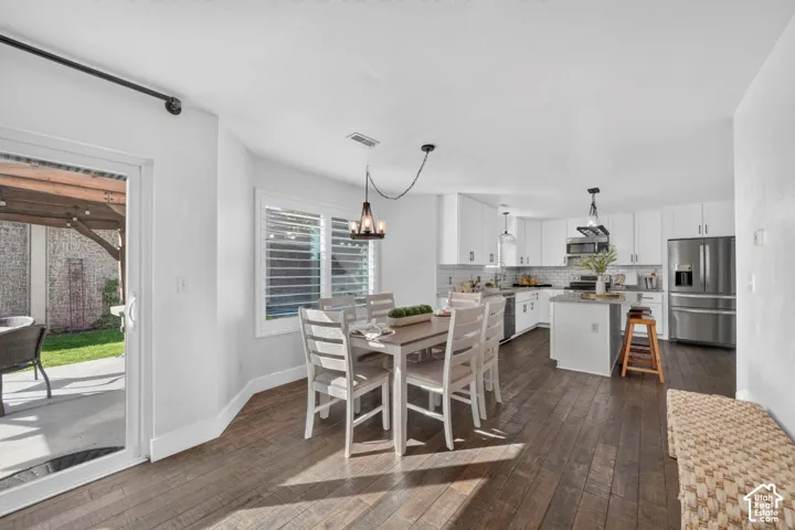 Wood-finish flooring, white cabinetry, stainless steel appliances, kitchen island with counter seating, and sliding glass door to the exterior