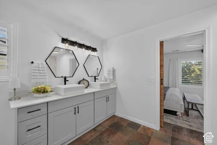 Dual vessel sinks with wall-mounted faucets, hexagon-shaped mirrors, gray cabinetry with matte black hardware, and slate-style floor tiling