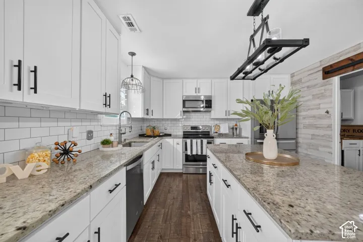White shaker-style cabinetry with matte black hardware, light-toned stone countertops, subway tile backsplash, and wood-finish flooring