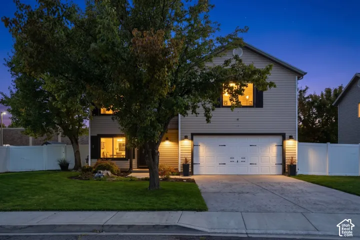Two-story residence featuring light-colored siding, a prominent two-car garage with decorative hardware, and a neatly maintained front lawn with mature trees