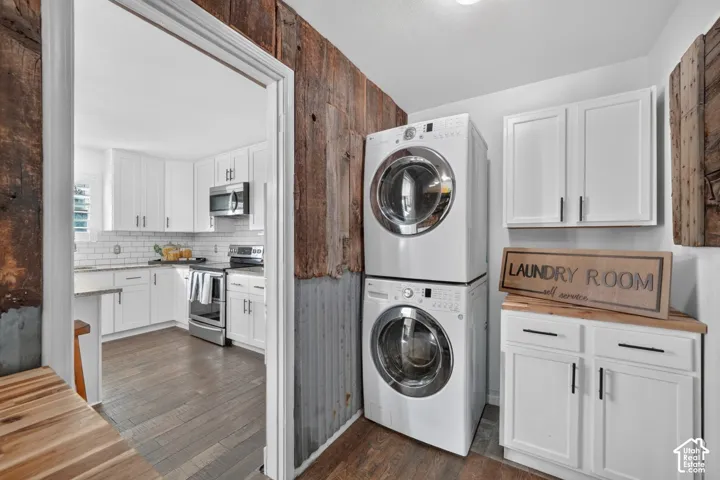 Laundry area with stacked appliances, white cabinetry, and wood-finish countertop
