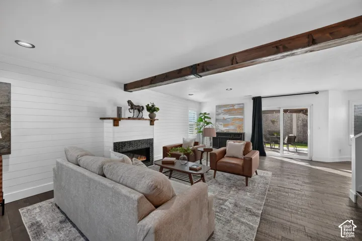 Living area featuring a fireplace with a dark tile surround, a wood mantel, shiplap accent wall, and a rustic wood ceiling beam