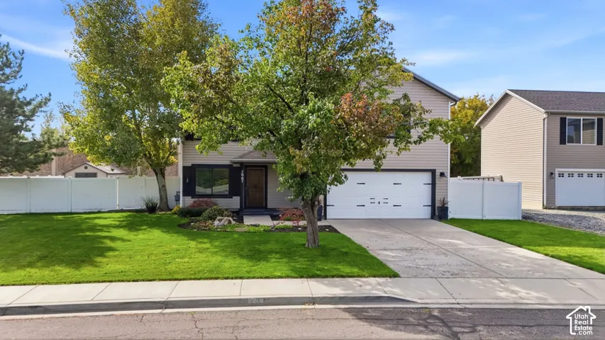 Two-story exterior with siding, attached garage, concrete driveway, and front lawn with mature trees