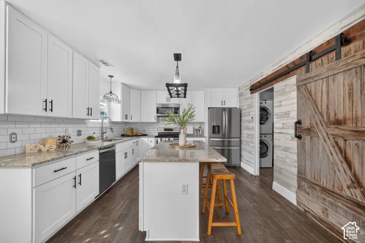 Bright kitchen featuring white cabinetry with dark hardware, a center island with a granite-style countertop, stainless steel appliances, and wood-finish flooring
