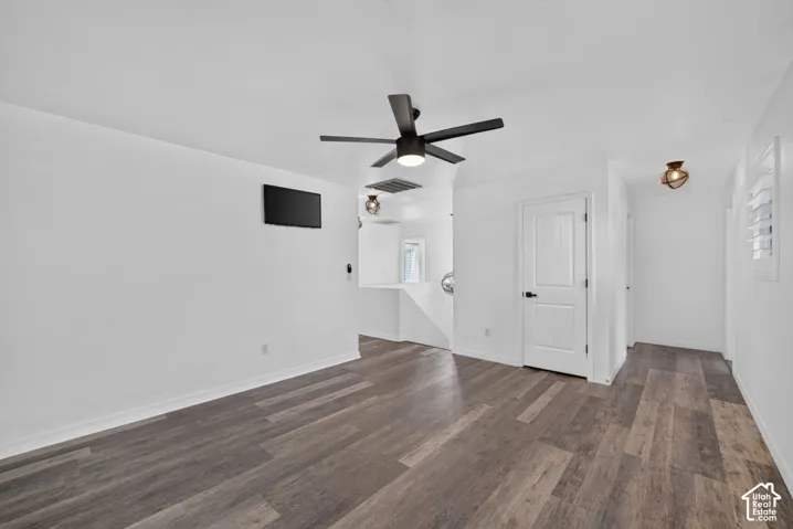 Wood-finish flooring, white walls, ceiling fan, white paneled door with black hardware, and shuttered window