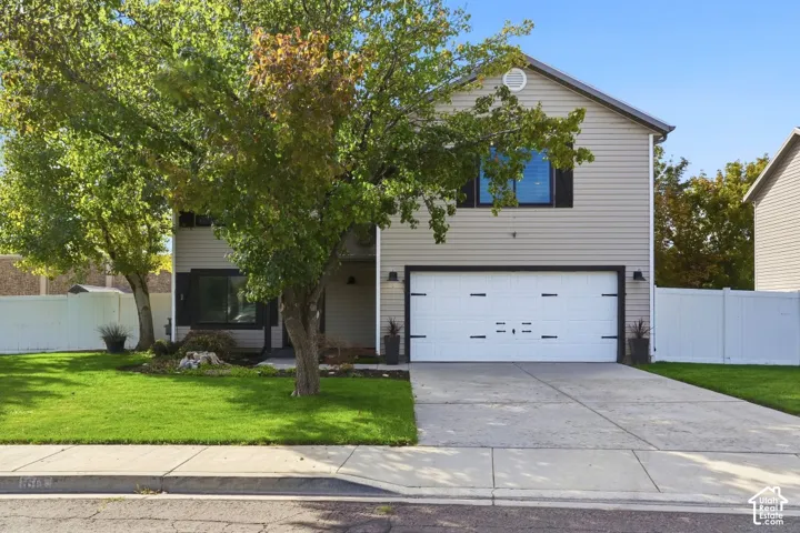 Two-story home with siding exterior, attached two-car garage, concrete driveway, front yard with mature trees, and a white fence